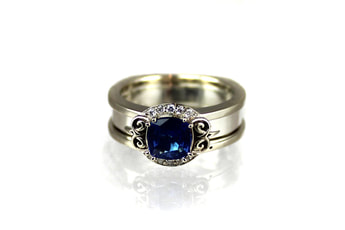 custom-designed sapphire engagement ring, cushion-cut sapphire, reverse-cradle ring, 14-karat white gold, ornate initials on shoulders, partial halo, beadset diamonds