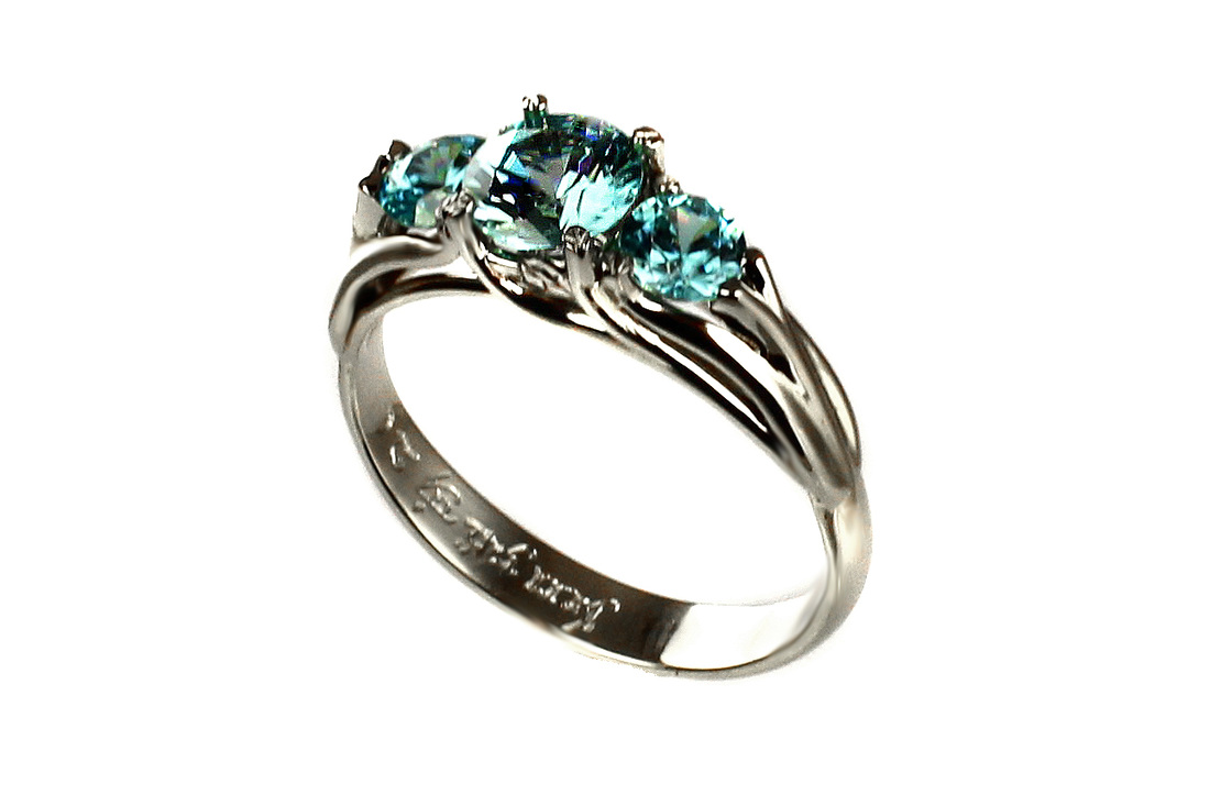 custom-designed fantasy engagement ring, blue zircon gemstones like crystal blue, three trees symbolism, weighted shank, inscription in Elfish